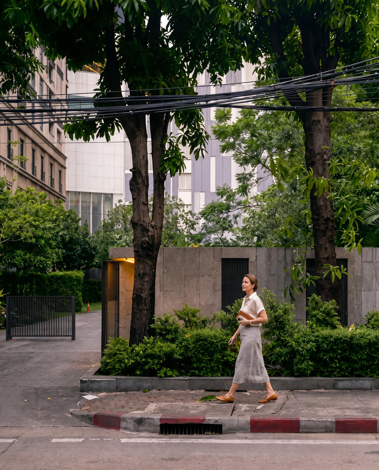 A person walking a residential Bangkok soi, with housing, trees and everyday street life around them.