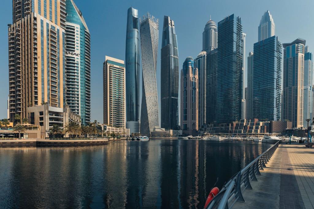 Dubai Marina skyline with twisted Cayan Tower and glass towers reflected in the marina water, seen from the waterfront promenade.