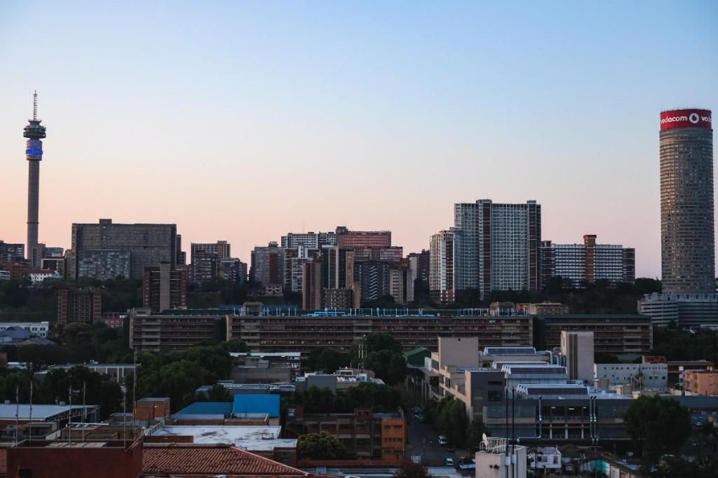 Johannesburg inner-city skyline at dusk with Hillbrow Tower, Ponte City and high-rise apartment blocks under a pale sunset sky.
