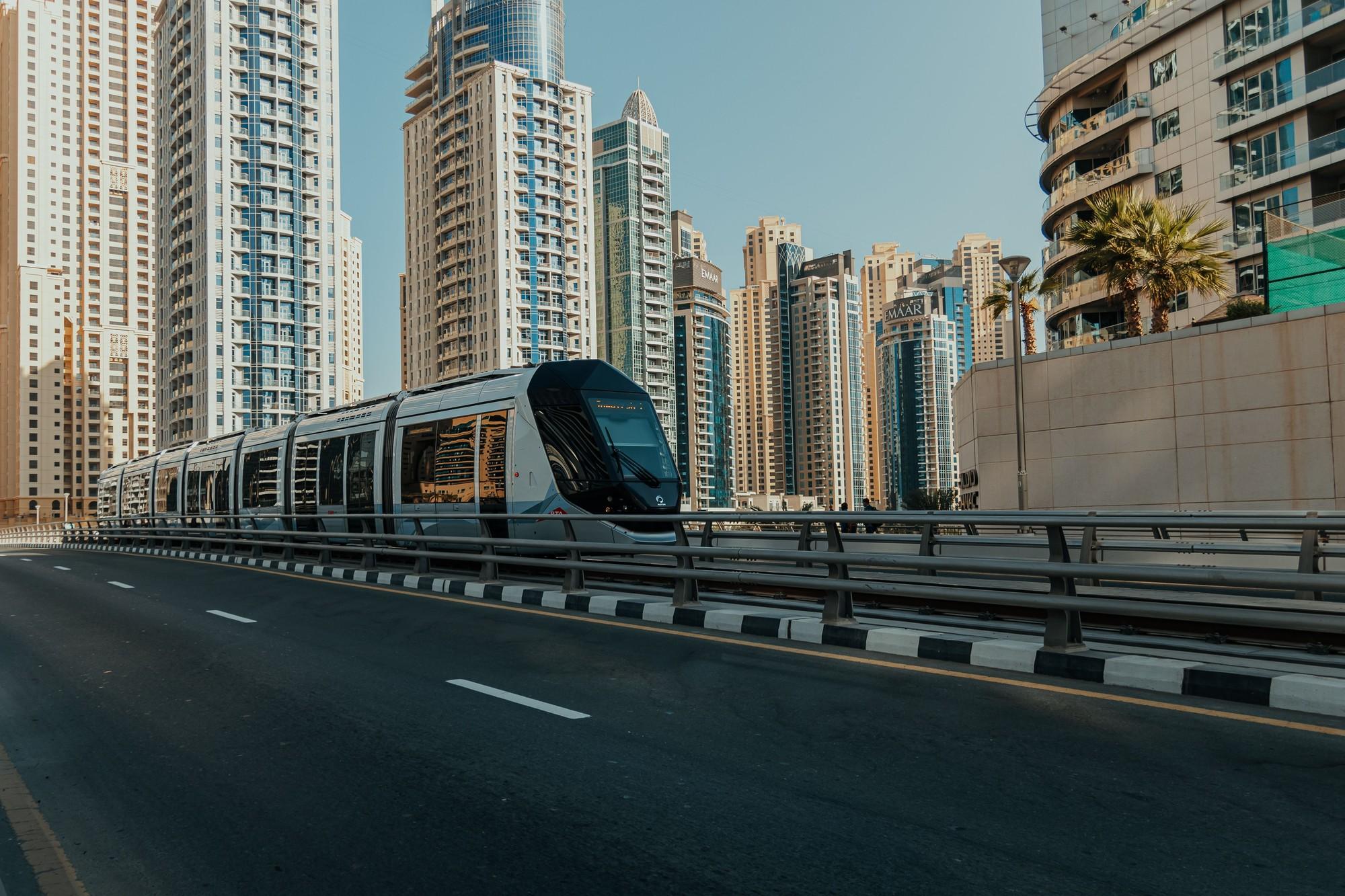 Dubai Tram moving through Dubai Marina/JBR with residential towers and road infrastructure.