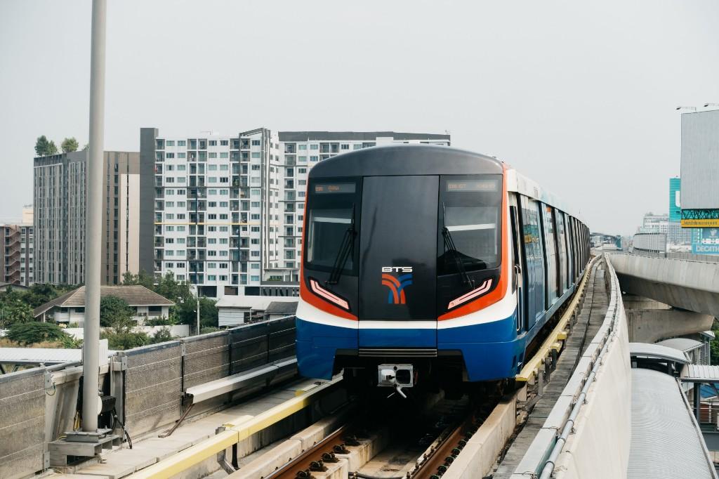 BTS Skytrain approaching on an elevated Bangkok track beside apartment buildings.