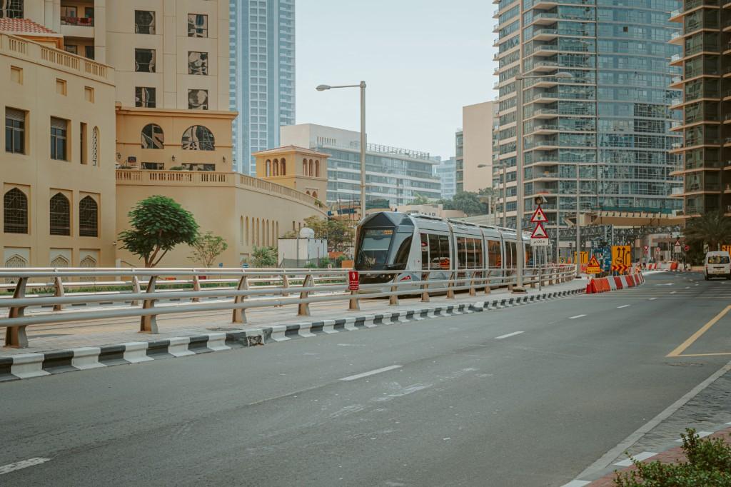 Weekday movement along a Dubai corridor with traffic, Metro access and hot-weather last-mile context visible.
